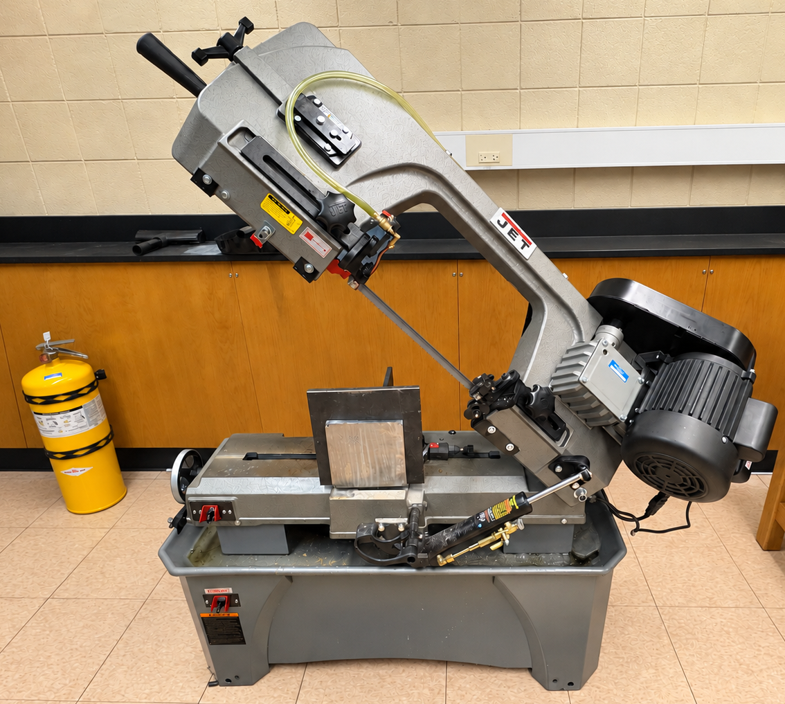 JET horizontal metal-cutting band saw on its coolant base in room E0040, with the saw head raised and a metal workpiece clamped in the vise.